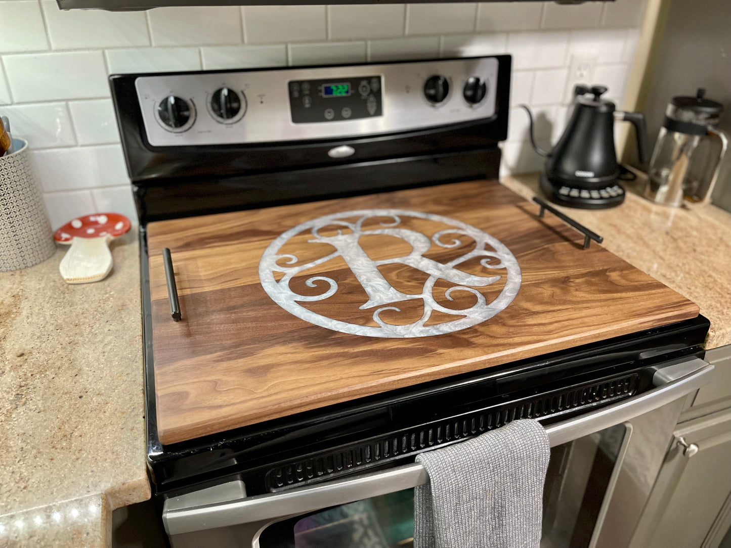 Wooden cutting board with a decorative monogram on an oven door in a kitchen.